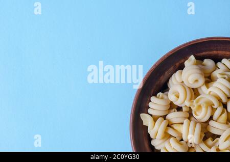 Serve pasta insalatonde non cotta in un recipiente su sfondo azzurro. Ingredienti della cucina mediterranea tradizionale. Gastronomia. Spazio di copia. Clos Foto Stock
