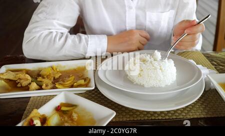 donna in camicia bianca sta mangiando riso. Sulla carne da tavola con verdure. Foto Stock