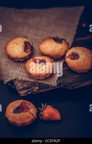 Cupcake con crema bianca e fragola su coperta d'annata su sfondo di legno nero con fragole fresche. Foto Stock