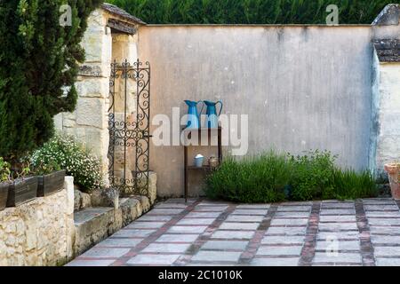 Cortile tradizionale francese giardino con pavimenti decorativi patio, piante, arbusti e due caraffe blu in metallo su un tavolo contro un alto muro, Loira Foto Stock