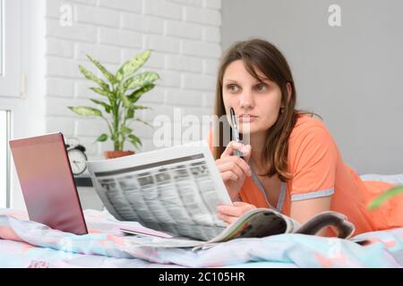 Ragazza che pensa mentre guardando gli annunci di lavoro di giornale Foto Stock