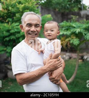 Nonno sorrise mentre trasportava il nipote in giardino durante il giorno Foto Stock