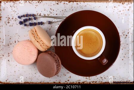 Primo piano tre biscotti alla francese e una tazza di caffè espresso serviti su un piatto marrone e su un piatto rustico in porcellana, vista dall'alto, direttamente ab Foto Stock