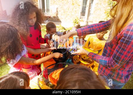 Un ritratto ravvicinato delle mani dei bambini di Halloween con i bambini in costumi da brivido riceve le caramelle di una donna che si trova vicino a casa insieme Foto Stock