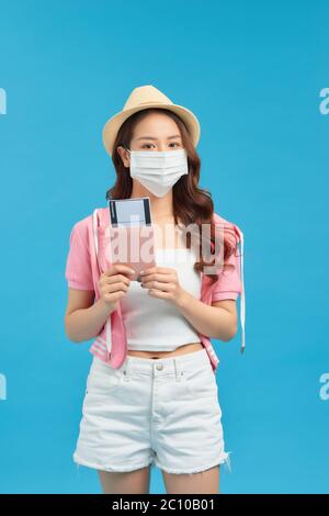 Giovane viaggiatore che indossa una maschera di cotone fatta a mano con passaporto e biglietto su sfondo blu. Concetto di viaggio durante il coronavirus. Foto Stock