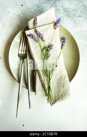 Tavolo estivo con posate e gres minimalistici serviti su fondo di cemento e decorato con fiori freschi di lavanda Foto Stock
