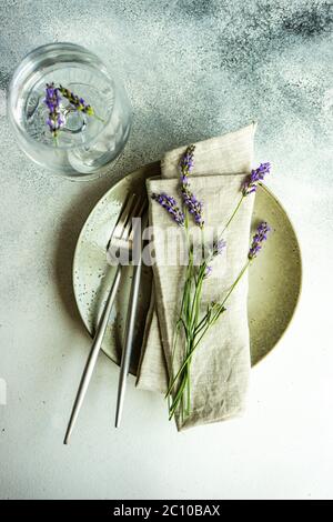 Tavolo estivo con posate e gres minimalistici serviti su fondo di cemento e decorato con fiori freschi di lavanda Foto Stock