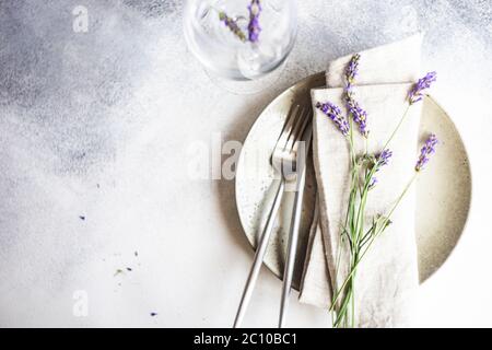Tavolo estivo con posate e gres minimalistici serviti su fondo di cemento e decorato con fiori freschi di lavanda Foto Stock