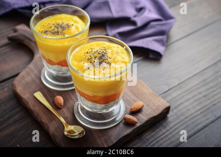 Budino di semi di chia fatto in casa con mango e mandorla in vetro su sfondo di legno Foto Stock