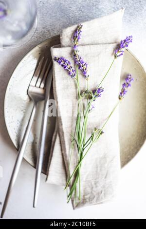 Tavolo estivo con posate e gres minimalistici serviti su fondo di cemento e decorato con fiori freschi di lavanda Foto Stock
