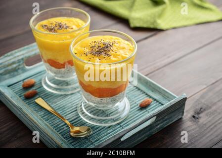Budino di semi di chia fatto in casa con mango e mandorla in vetro su sfondo di legno Foto Stock