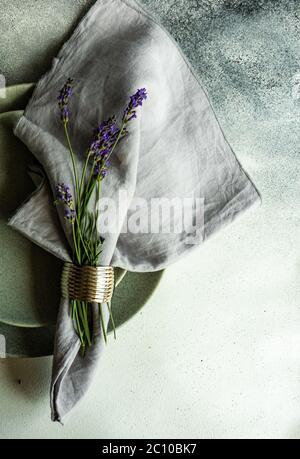 Tavolo estivo con posate e gres minimalistici serviti su fondo di cemento e decorato con fiori freschi di lavanda Foto Stock