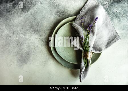 Tavolo estivo con posate e gres minimalistici serviti su fondo di cemento e decorato con fiori freschi di lavanda Foto Stock