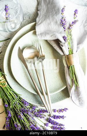 Tavolo estivo con posate e gres minimalistici serviti su fondo di cemento e decorato con fiori freschi di lavanda Foto Stock