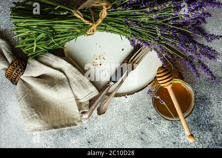 Tavolo estivo con posate e gres minimalistici serviti su fondo di cemento e decorato con fiori freschi di lavanda Foto Stock
