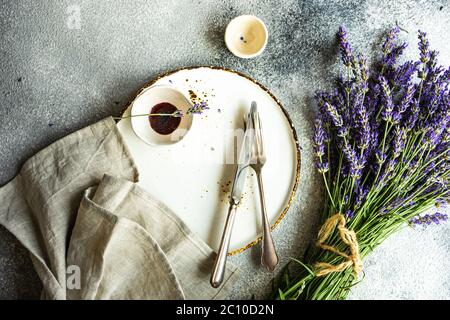 Tavolo estivo con posate e gres minimalistici serviti su fondo di cemento e decorato con fiori freschi di lavanda Foto Stock