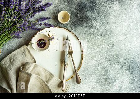 Tavolo estivo con posate e gres minimalistici serviti su fondo di cemento e decorato con fiori freschi di lavanda Foto Stock