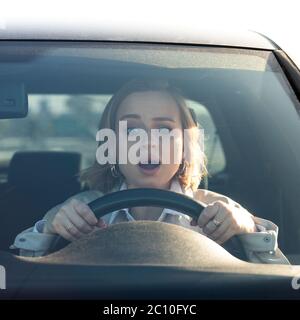 Donna in stress e confusione dopo un incidente, ha danneggiato un'altra auto durante il parcheggio, guida la sua auto per la prima volta. Conducente con bocca aperta e ast Foto Stock