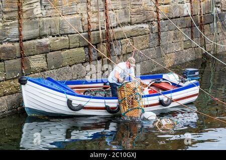 Pescatore che prepara le creelle di aragosta prima di uscire a pescare nella sua piccola barca aperta, Dunure, Ayrshire, Scozia, Regno Unito Foto Stock