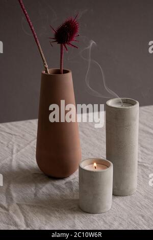 Composizione in stile igge composta da candele bruciate e soffiate in vetri di ceramica bianca e vaso di argilla marrone fatto a mano con due fiori secchi Foto Stock