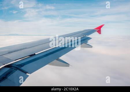 Ala di un aereo con lembi abbassati su uno sfondo di cielo blu e mare di nuvole bianche sottostanti. Foto Stock