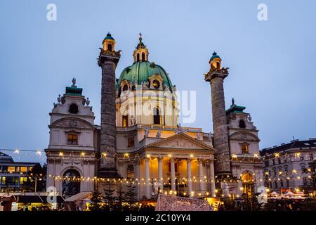 Vista notturna di Karlskirche (Chiesa di San Carlo) e le luci del mercatino di Natale di fronte. Vienna, Austria Foto Stock