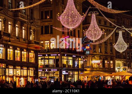 Vista notturna di via Graben con luci natalizie, finestre illuminate dei negozi, grandi lampadari sospesi e molti turisti a piedi, Vienna. Foto Stock
