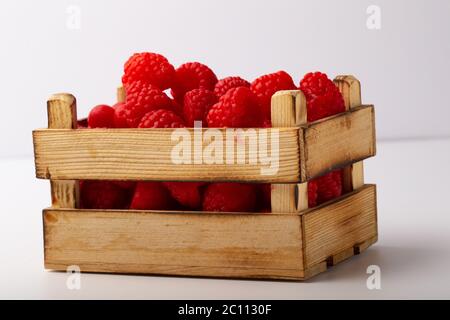 Alcuni lamponi in una piccola scatola di legno su sfondo bianco Foto Stock
