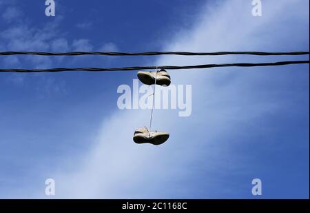 paio di sneakers appesi su fili un cielo blu di sfondo vicino alla scuola della città Foto Stock