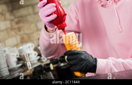 barista aggiungendo salsa al ketchup in francese hot dog con salsiccia alla griglia Foto Stock