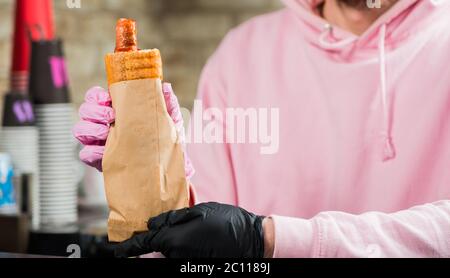 barista che tiene il cane caldo francese con salsiccia alla griglia in confezione di carta Foto Stock