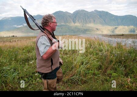 Un cacciatore che tiene una fucile e indossa i waders da pesca in un estuario del torrente nella Great Bear Rainforest, vicino a Bella Coola, British Columbia, Canada. Foto Stock