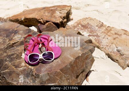 Scarpe rosa con infradito e occhiali da sole alla moda sulla roccia della spiaggia. Concetto estivo. Foto Stock