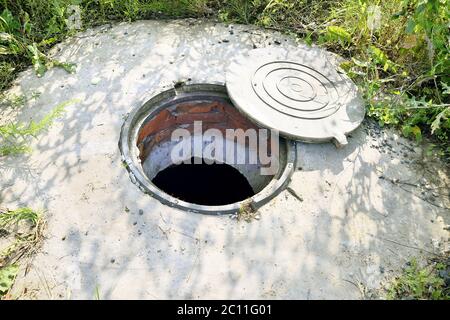 Cesspit di cemento con un portello aperto sul terreno in estate Foto Stock