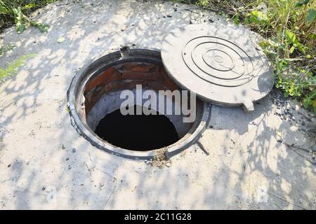 Cesspit di cemento con un portello aperto sul terreno in estate Foto Stock