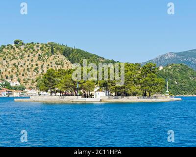 Una piccola chiesa imbiancata sorge sull'isolotto di Lazareto, vicino a vithi sull'isola di Ithaka, circondata da alberi. Foto Stock