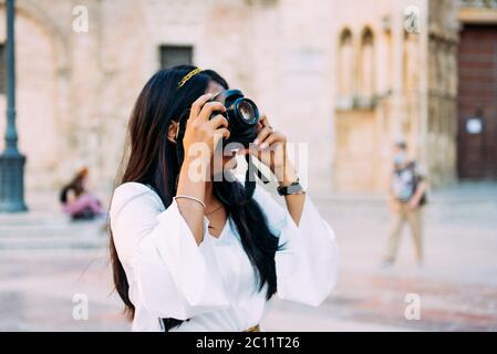 Donna di brunetta latina vestita in bianco passeggiando per la città con fotocamera, concetto di viaggio Foto Stock