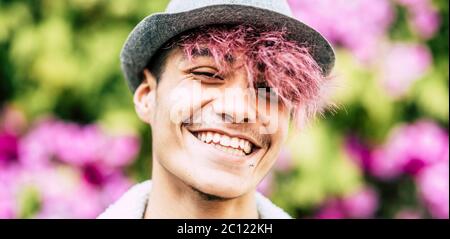 Felice allegro bel ritratto trendy alternativo giovane uomo adolescente sorridente su macchina fotografica con sfondo colorato parco di fiori - diversità e giovane Foto Stock