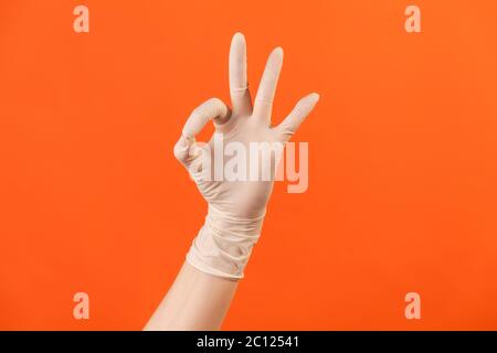 Profilo Vista laterale primo piano della mano umana in guanti chirurgici bianchi con il segno OK o il numero 3 con le dita. Interno, studio shot, isolato su bac arancione Foto Stock