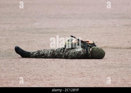 Uomo in camuffamento militare abbigliamento e una maschera che si trova sulla schiena la sabbia con mitragliatrici in mano durante la dimostrazione Foto Stock