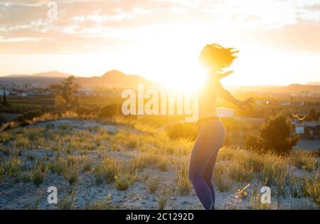 Giovane donna attraente che gira a braccia aperte sulla cima della montagna contro il tramonto. Carino caldo ragazza improvvisa e godere di fredoom in natura mentre sorridendo e. Foto Stock