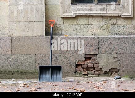 Nuova pala nera con manico arancione si appoggia contro il muro del palazzo in attesa di autorizzazione dal vicolo caduto lasciare Foto Stock