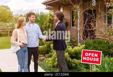 Nuovi proprietari di casa scuotendo le mani con agente immobiliare vicino edificio residenziale esterno, spazio di copia Foto Stock