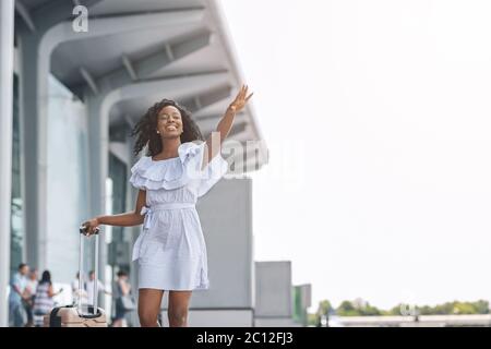 Prendere un taxi. Giovane donna nera che cerca di prendere un taxi vicino all'edificio dell'aeroporto Foto Stock