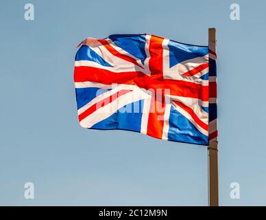 Un Union Jack sventola vigorosamente nel vento contro un cielo blu nell’East Suffolk, Inghilterra. Foto Stock