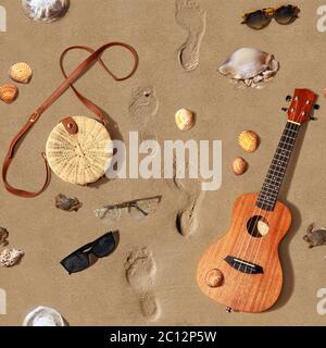 Sfondo senza cuciture. Composizione estiva con ukulele, borsa, occhiali da sole, conchette e meduse su una spiaggia di sabbia. Rosignano Solvay. Italia. Foto Stock