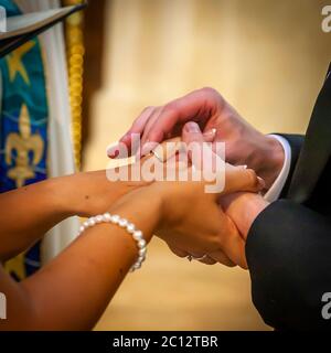 Gli sposi si tengono per mano durante lo scambio delle fedi. Uno stendardo chiesa blu e oro con un motivo a stelle è visibile in fondo. La fotografia mostra lo scambio delle fedi durante il servizio matrimoniale anglicano nel South Cambridgeshire, Inghilterra. Foto Stock