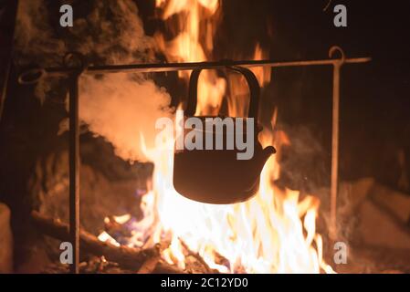 Il bollitore viene riscaldato su un fuoco acceso di notte all'aperto Foto Stock