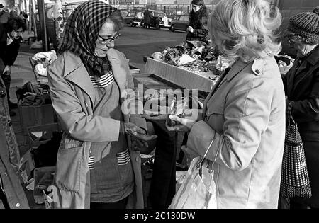 AJAXNETPHOTO. 27 FEBBRAIO 1975. PORTSMOUTH, INGHILTERRA. - MERCATO DELLE PULCI - IN STRADA UNICORN; UN ACQUIRENTE CONSEGNA ALCUNE MONETE AL COMMERCIANTE DI STRADA (SINISTRA).PHOTO:JONATHAN EASTLAND/AJAX REF:7513 25A 110 Foto Stock