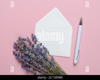 Buquet di lavanda profumata in fiore su una busta bianca e penna a sfera su uno sfondo rosa di texture. Biglietto d'auguri romantico estivo. Spazio di copia. Foto Stock